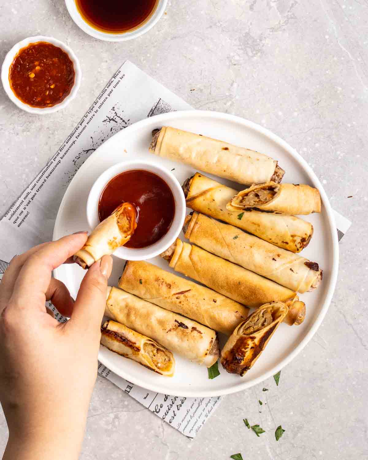 A hand dipping a vegan lumpia into sauce