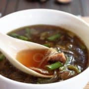 A white spoon scooping some dark onion and mushroom soup.