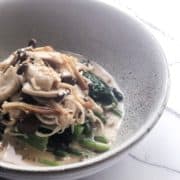 A white bowl full of marinated mushrooms.