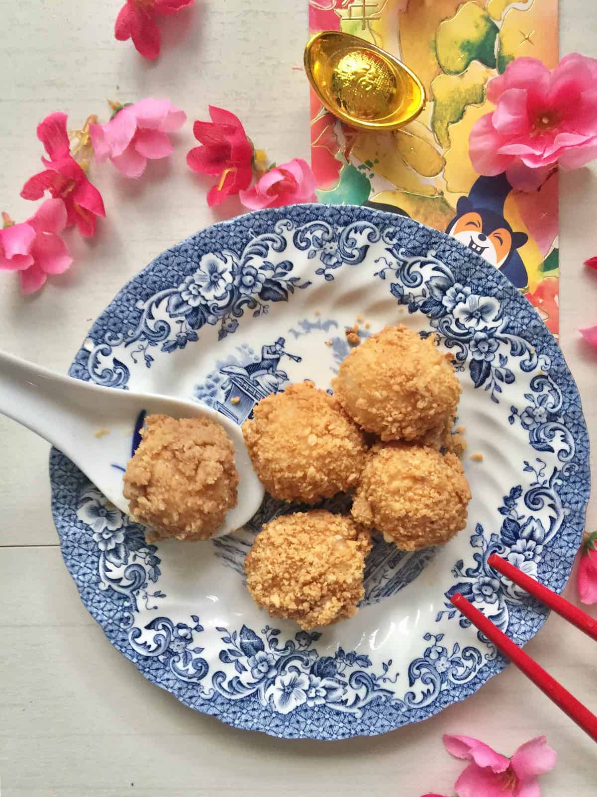 4 glutinous rice dumpling balls coated with ground roasted peanut on a blue and white plate wit Chinese New Year decor all around