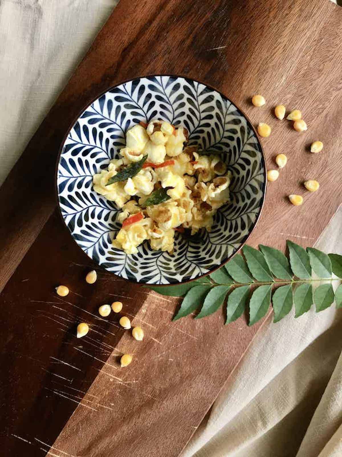 A bowl of homemade stovetop popcorn with corn kernels around it.