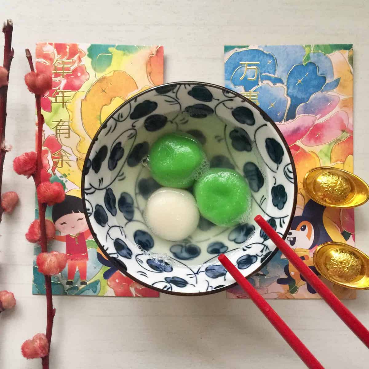 2 green pandan plain tang yuan and 1 filled with sesame in a bowl of ginger longan soup.