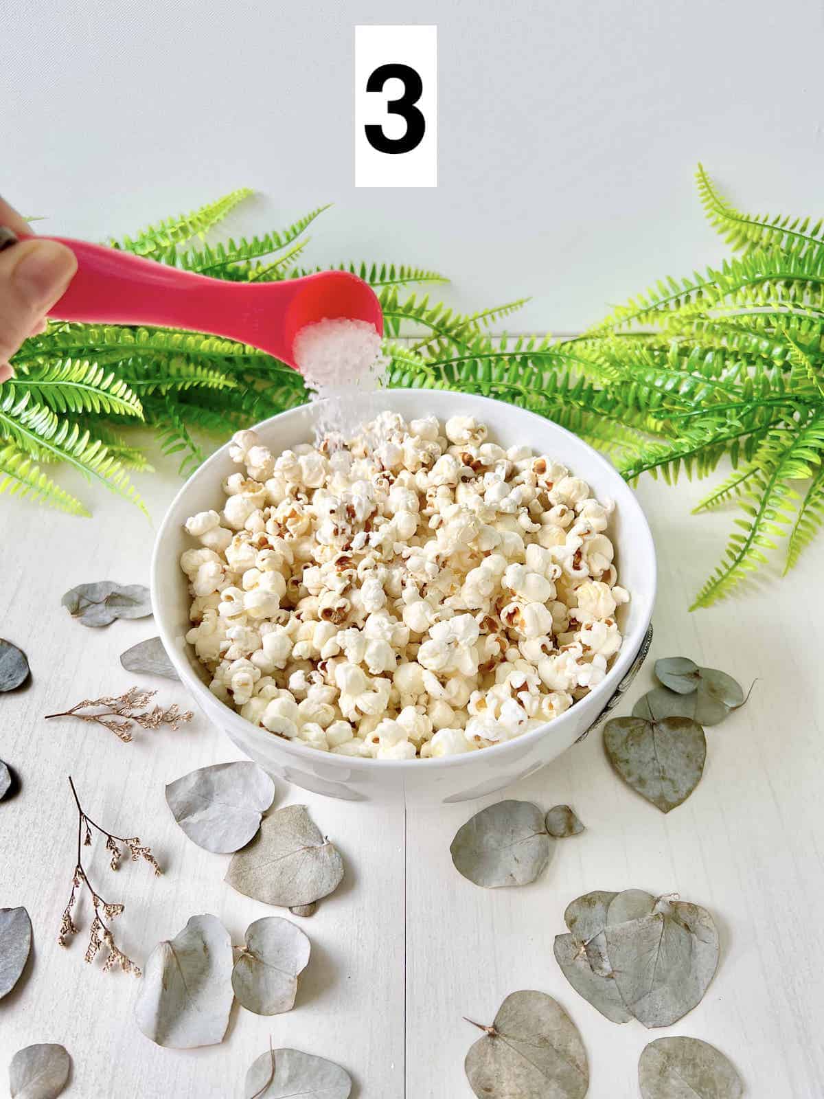 A spoonful of salt being added to fresh stovetop popcorn.