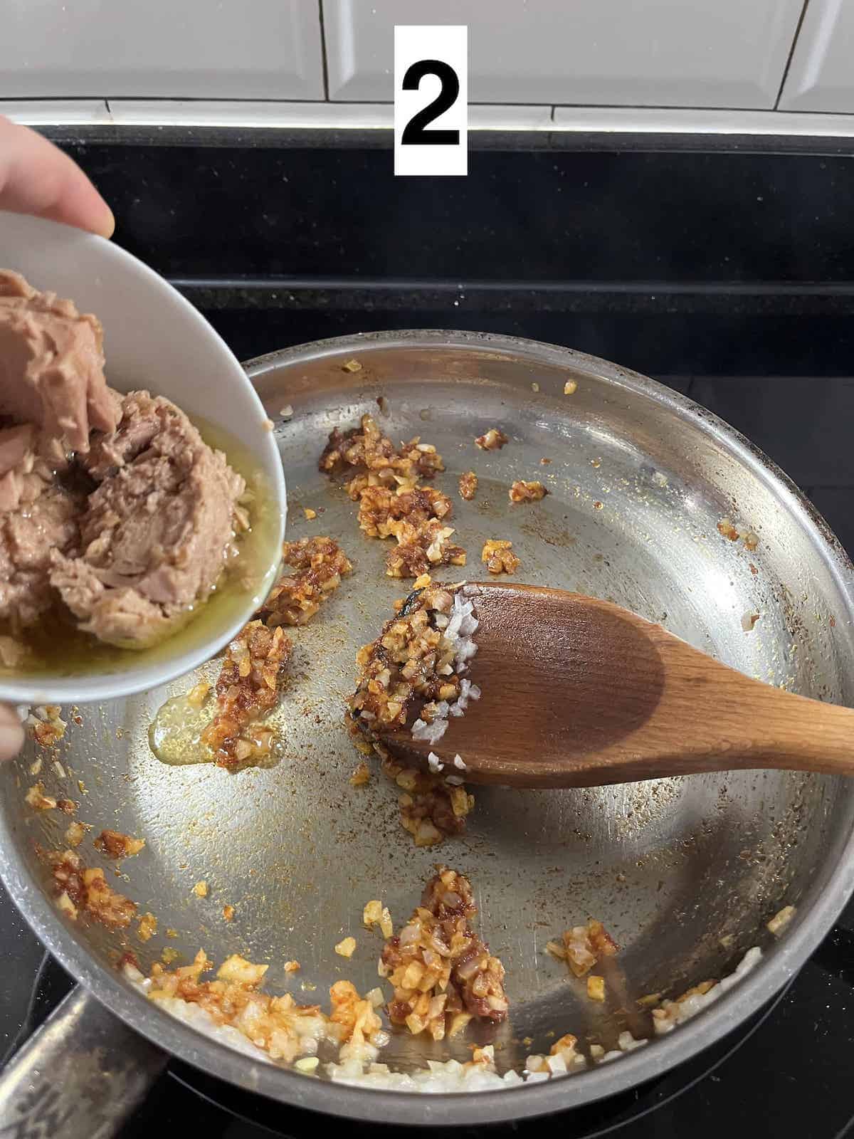 Adding canned tuna to a pan with sambal onions.