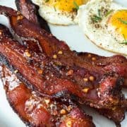 Candied bacon on white plate with sunny side eggs