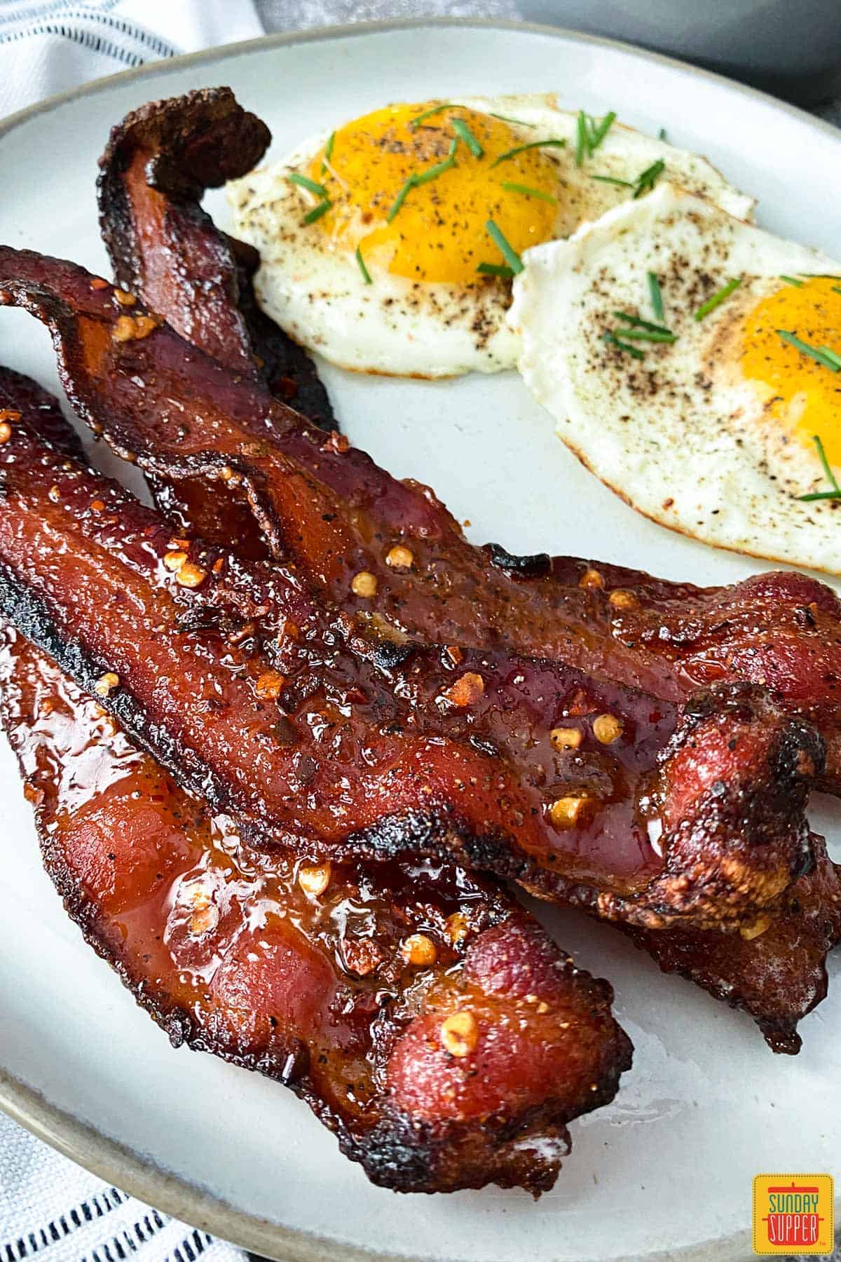Candied bacon on white plate with sunny side eggs