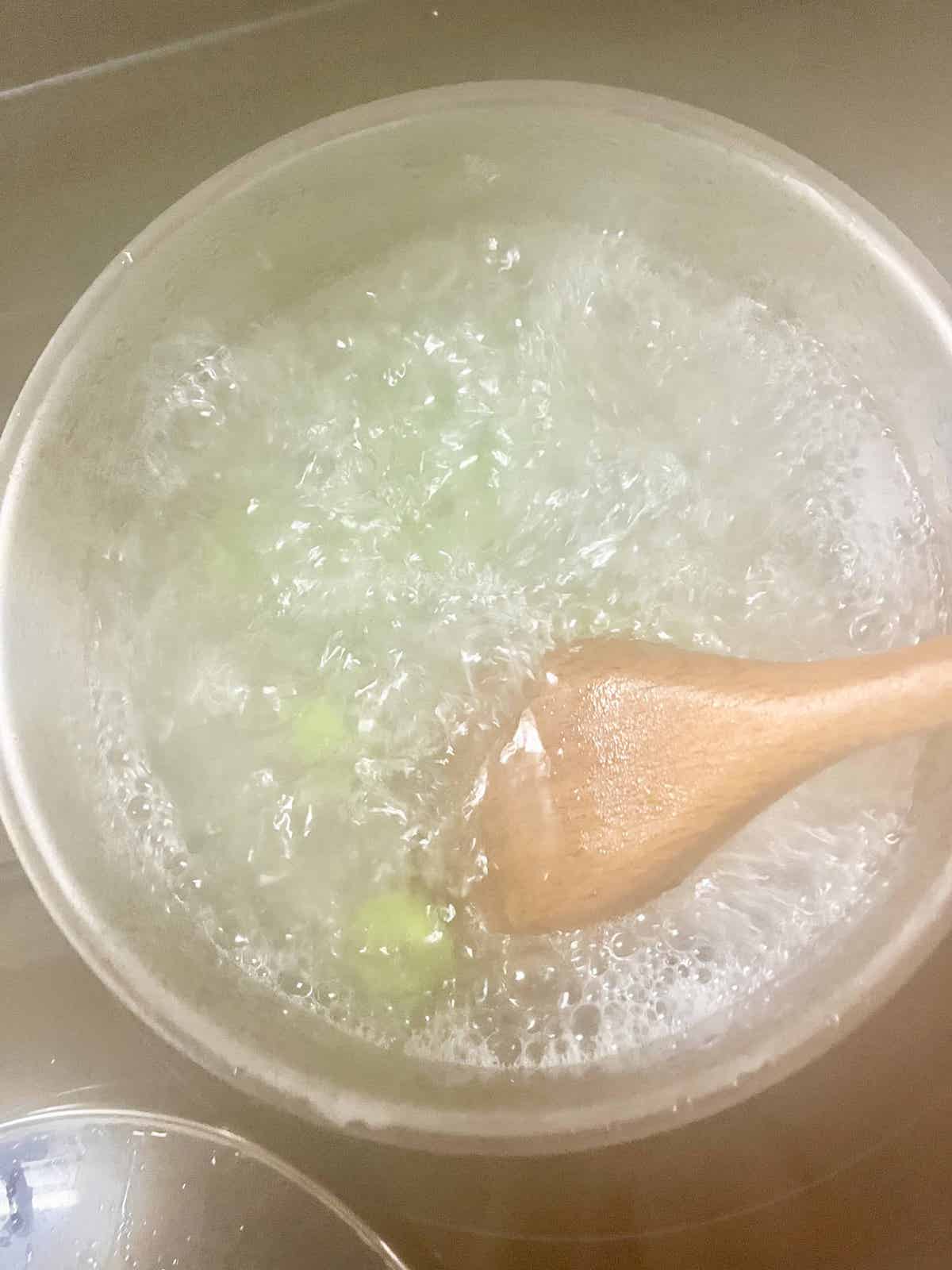 Pandan tang yuan being cooked in a boiling pot of water.