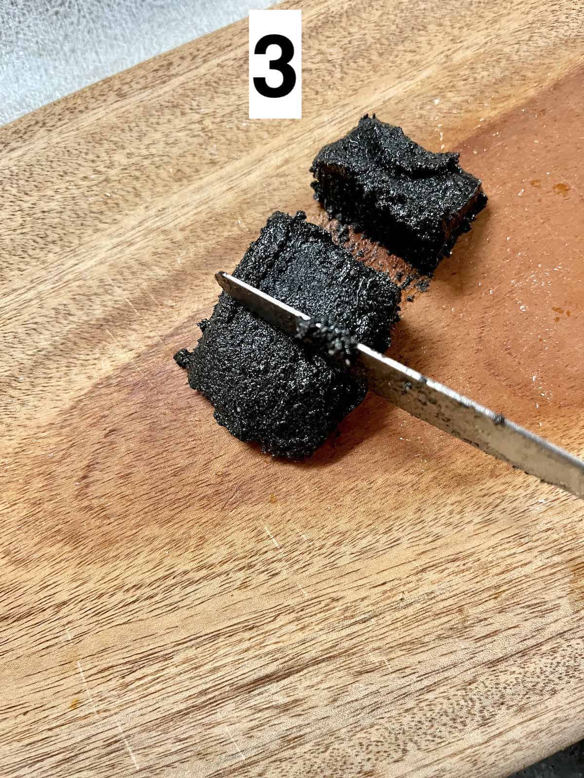 A small block of black sesame being cut into 3 pieces.