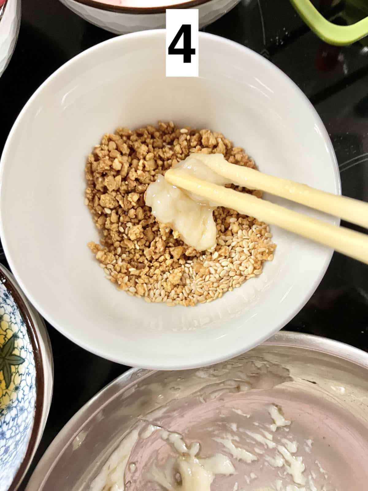 Dipping muah chee dough in peanuts and white sesame seeds.