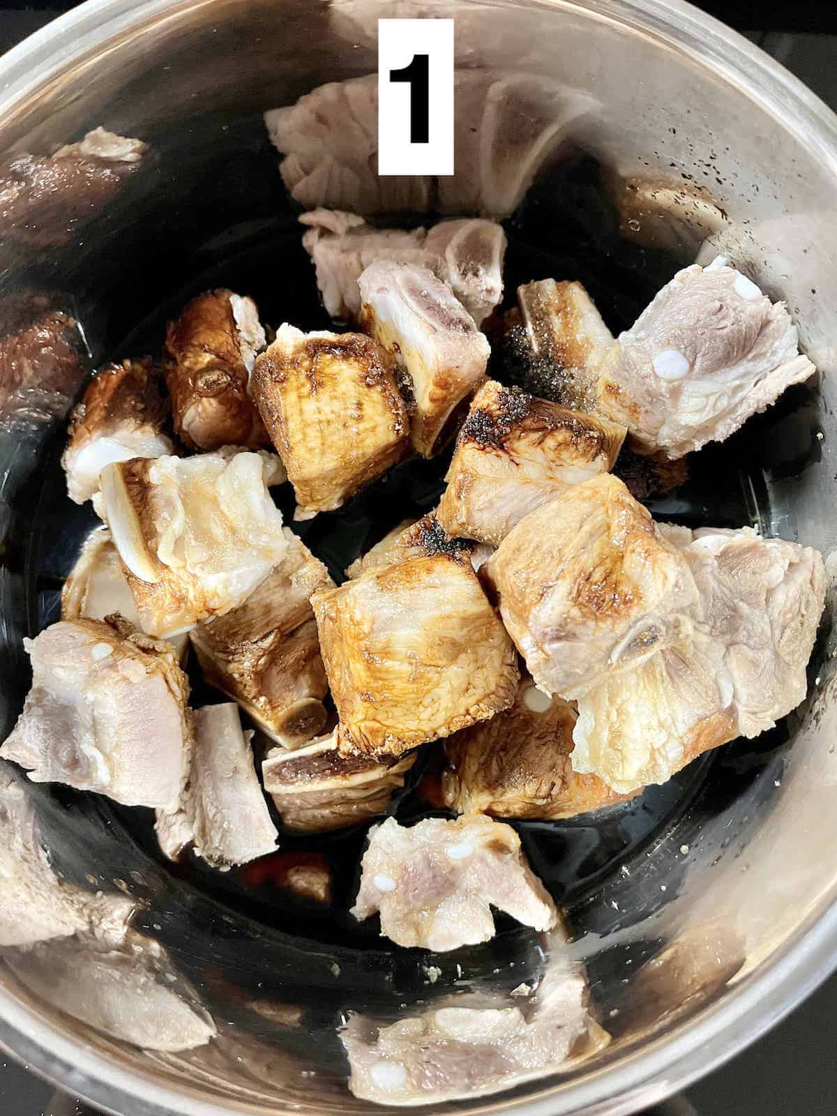 Close-up of pork ribs in a silver pot with sauce around.