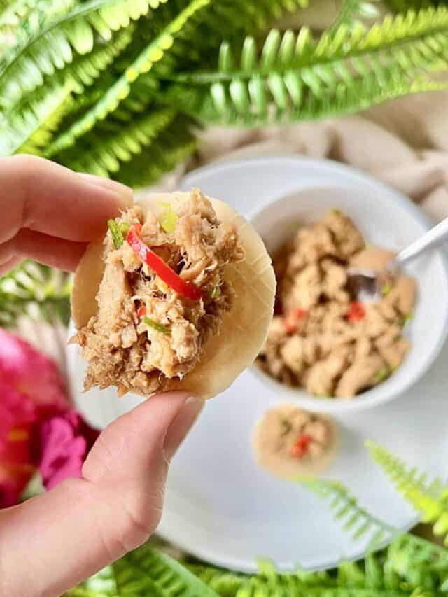 Close-up of a hand holding a cracker with spicy canned tuna dip on it.