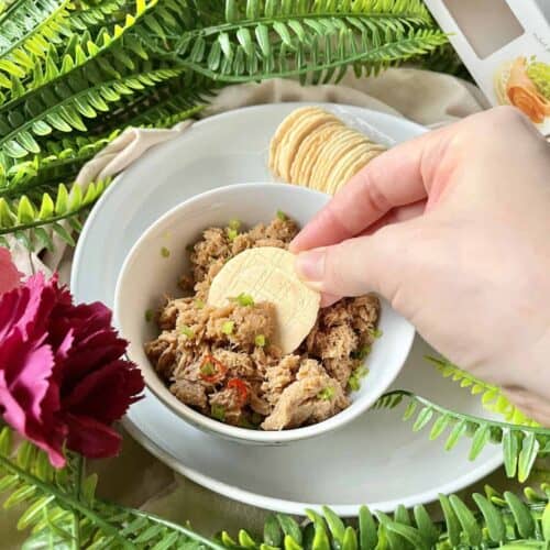 Someone dipping a cracker into a bowl of spicy coconut tuna curried dip.