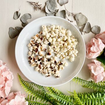 A white plate full of stovetop popcorn surrounded by flowers and leaves.