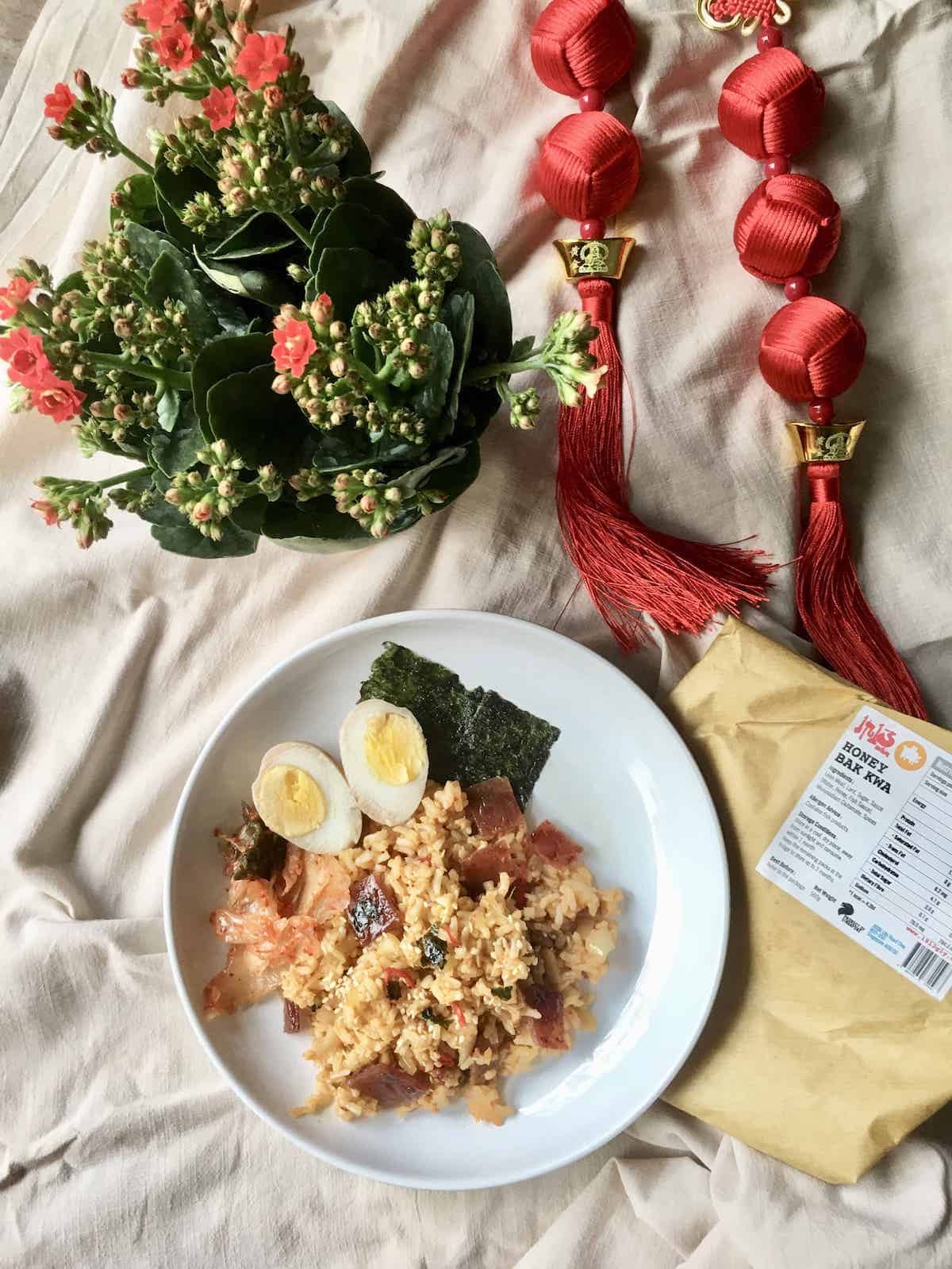 A plate of kimchi fried rice made with leftover bak kwa surrounded by Chinese New Year decor.