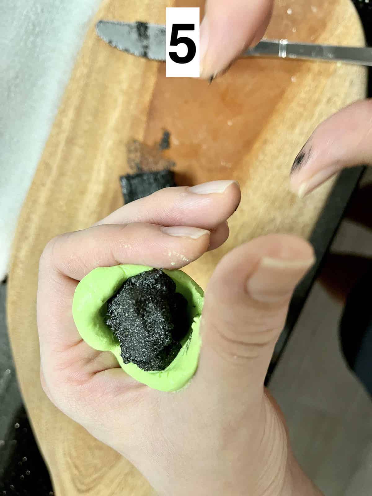 A block of black sesame paste inside a circular piece of green glutinous dough.