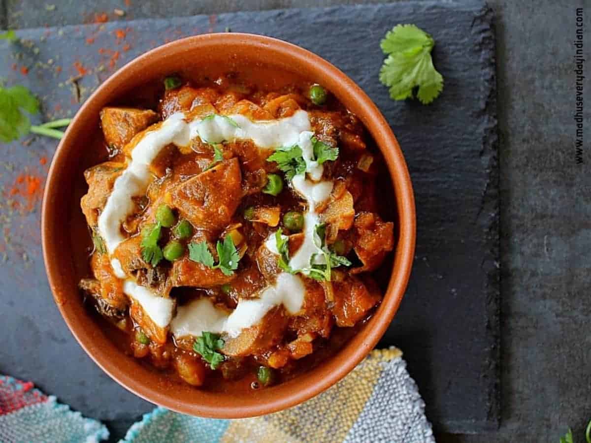 A bowl of red mushroom masala in an orange bowl.