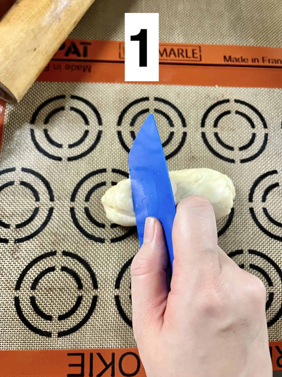 Using a dough scraper to cut the log of dough.