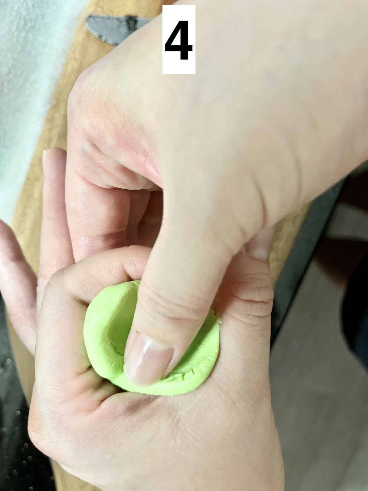 A thumb pressing a hole into a ball of green dough.