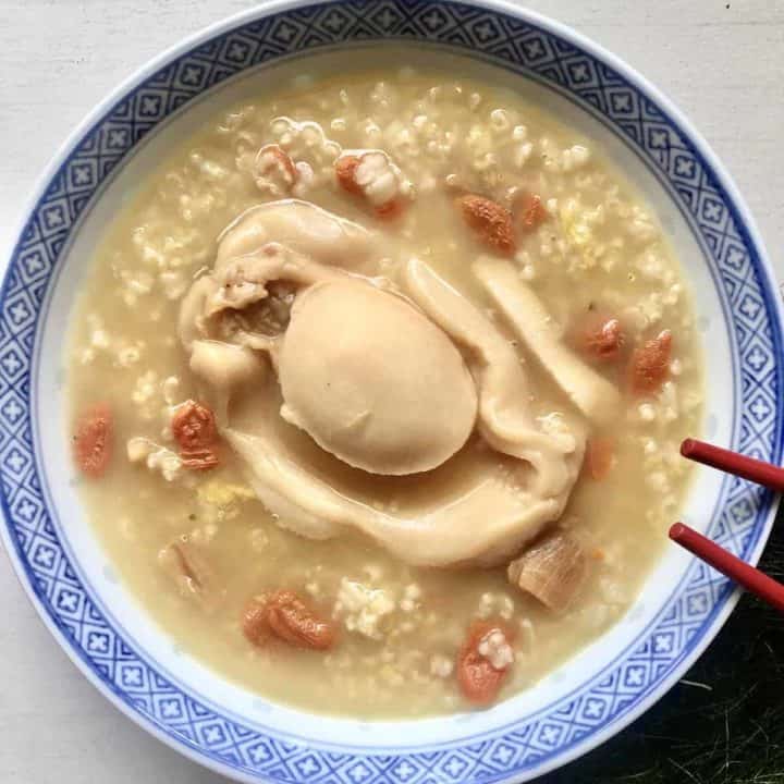 Close-up of a bowl of chicken porridge with a huge abalone on top.