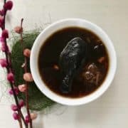A bowl of Chinese black chicken soup with red dates, goji berries, scallops and dried shiitake mushrooms.
