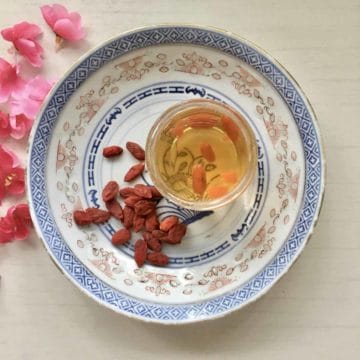 A cup of wolfberry tea with dried goji berries next to it.