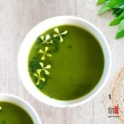 A bowl of green soup with some flower decorations on top.