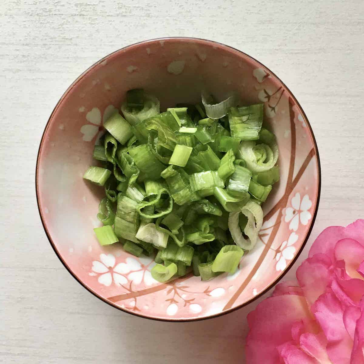 A bowl of sliced spring onions, top green part only.