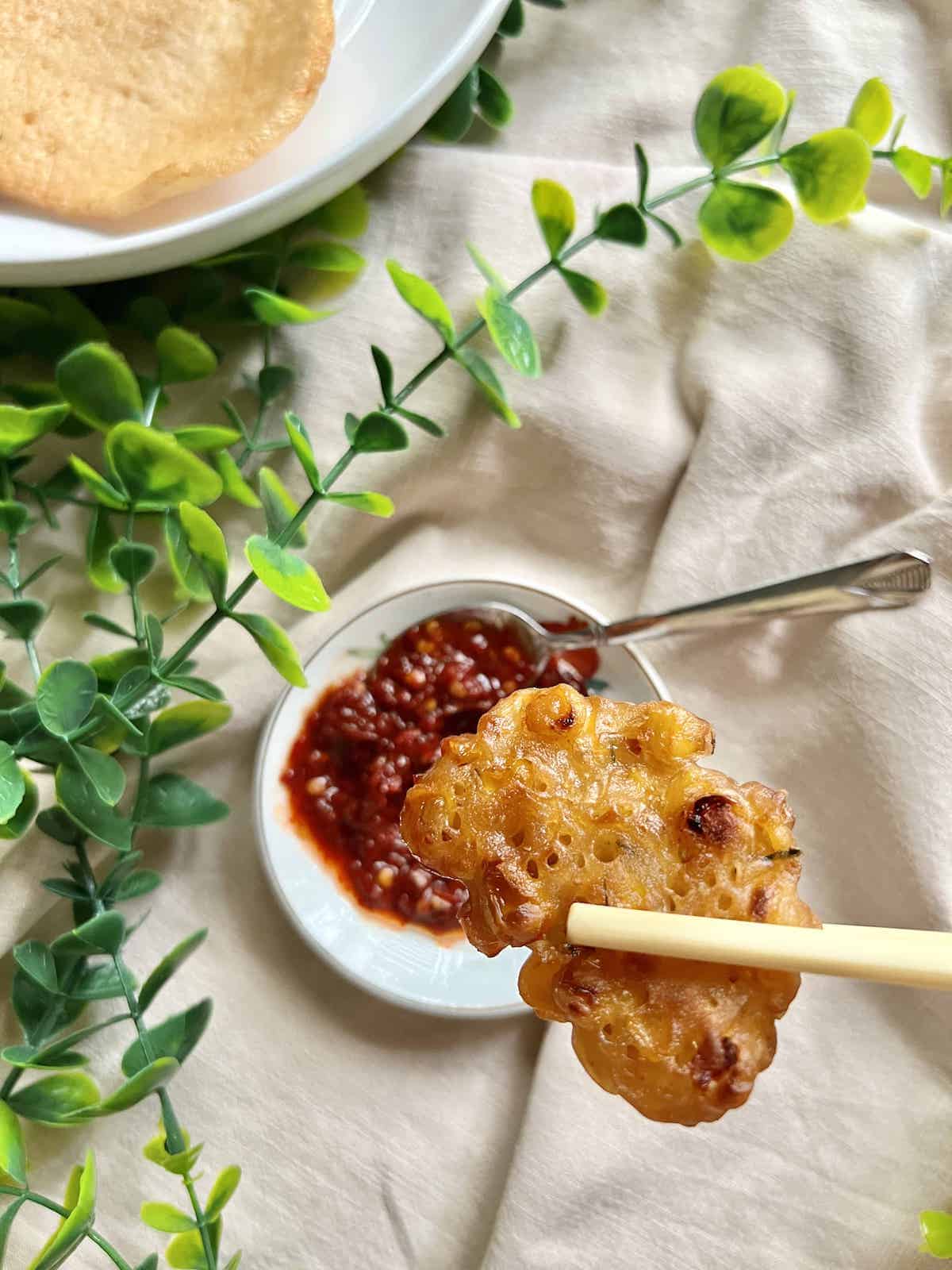 An Asian corn fritter being dipped into a platter of Sambal Oelek sauce.