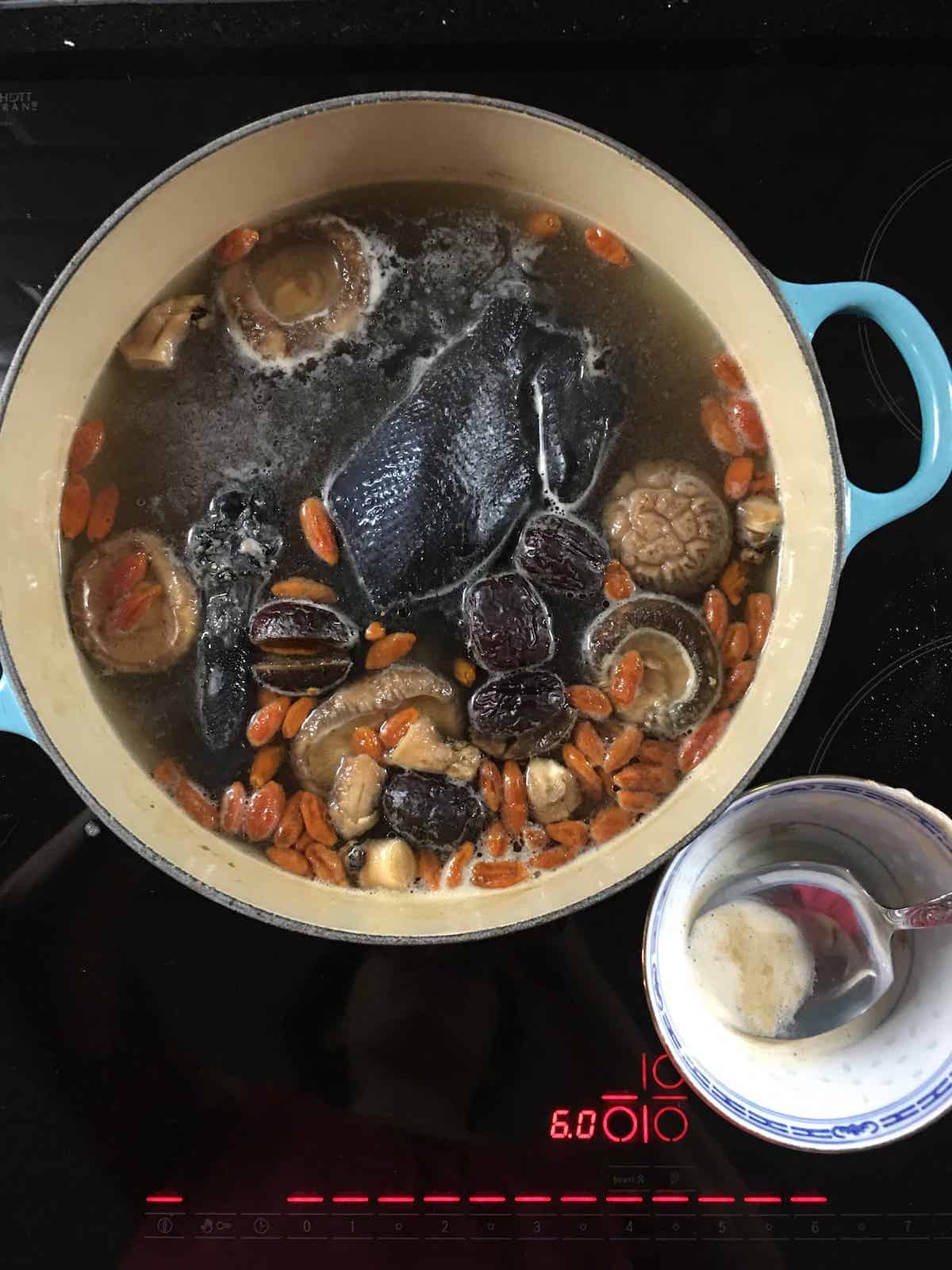 Cantonese black chicken soup that is having the scum removed as it boils.