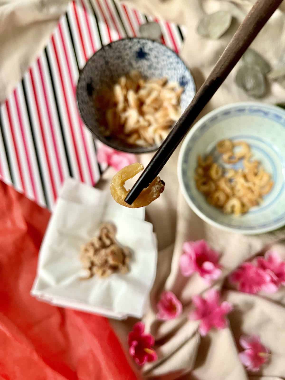 A dried shrimp held up by a pair of chopsticks.