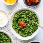 A big bowl of green palm Khichdi on a table with other food.