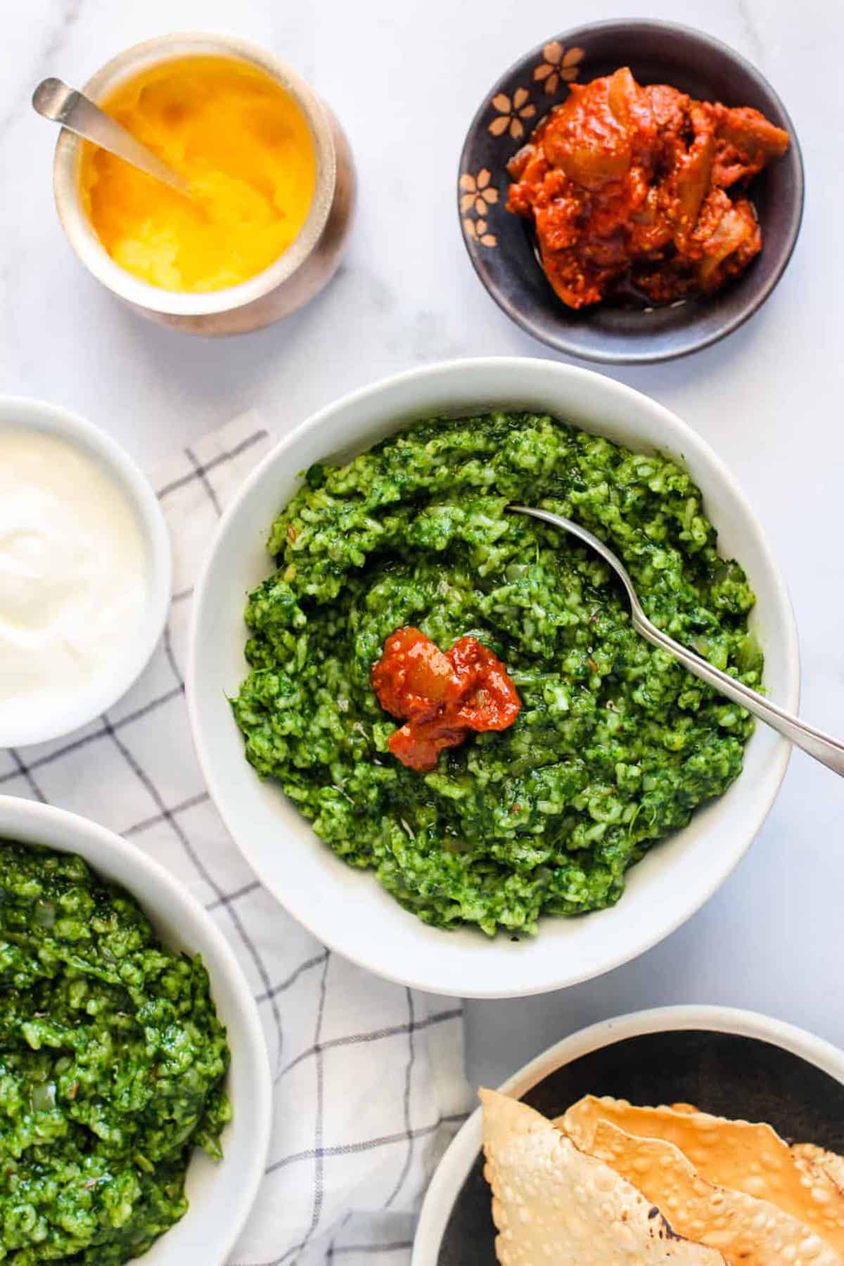 A big bowl of green palm Khichdi on a table with other food.