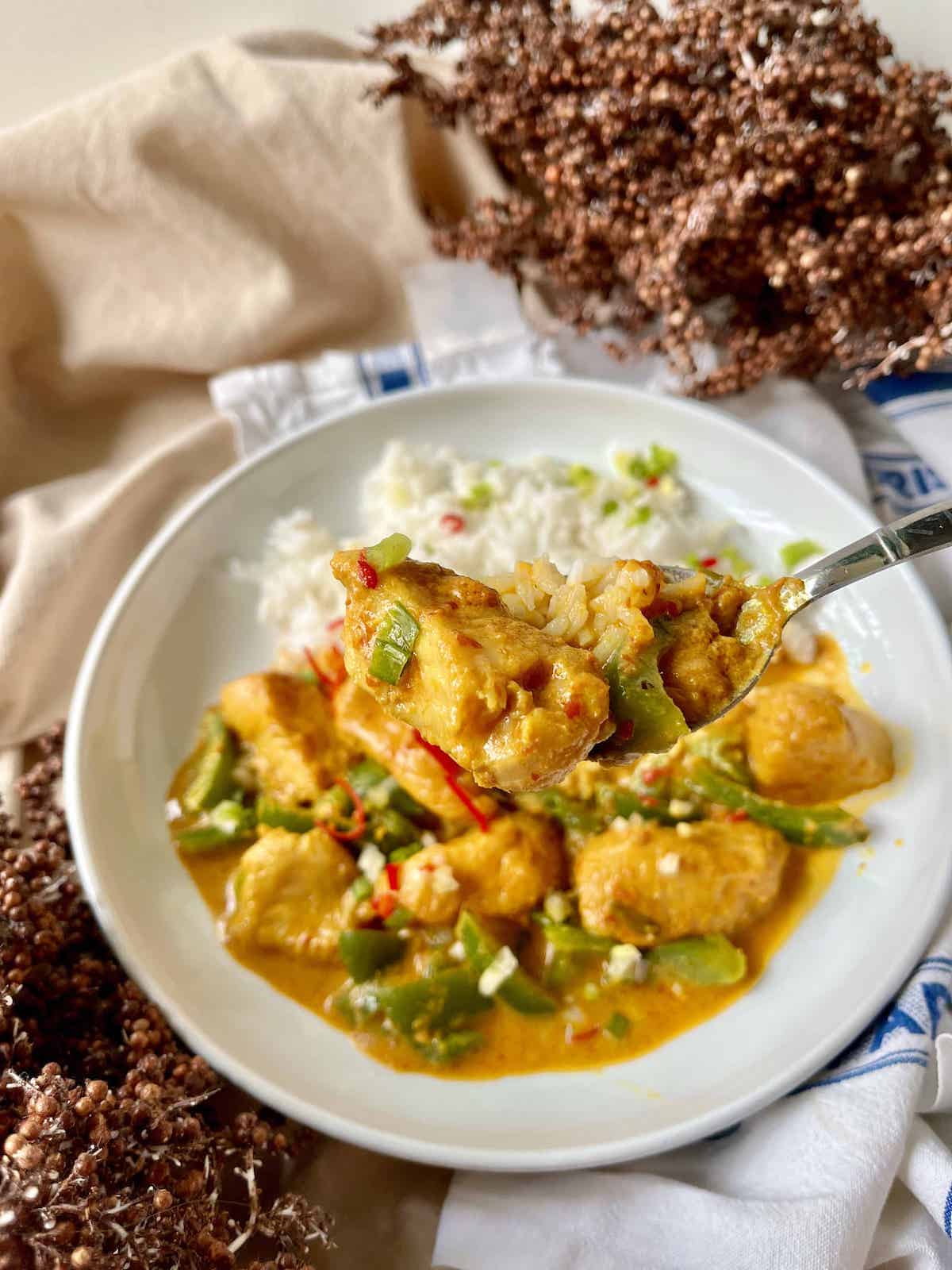 Someone scooping up a bite of simmered fish in coconut milk and jasmine rice.