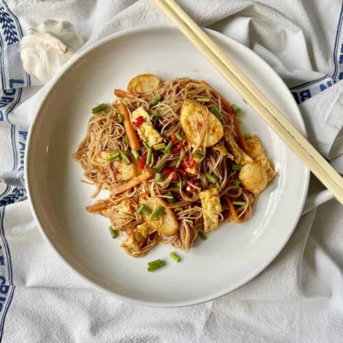 A plate of Singaporean fried vermicelli noodles with egg, carrot and fish cake.