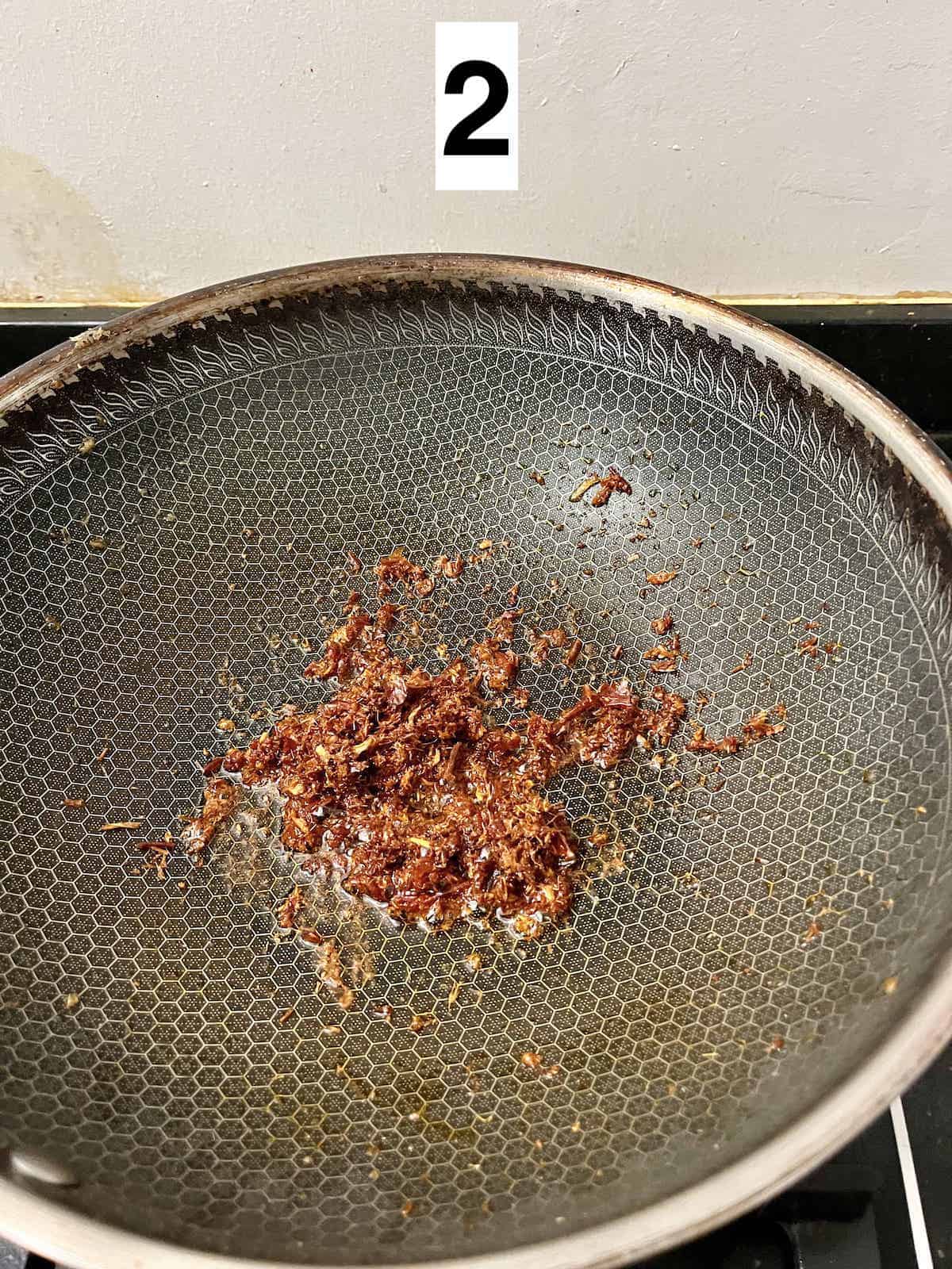 Blended aromatics and dried chilies being stir-fried in a pan.