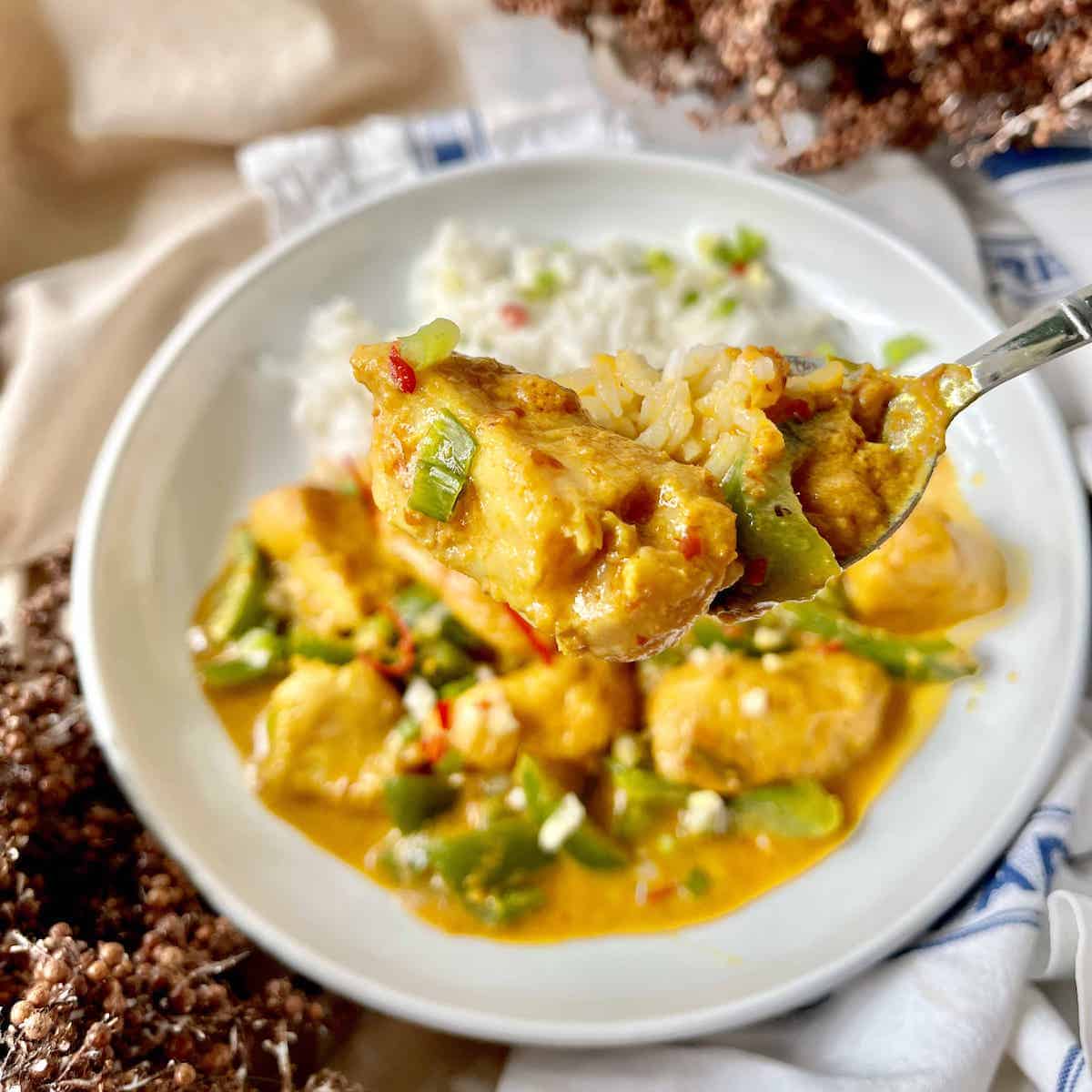 Close-up of a white plate of tamarind fish curry with coconut and rice.