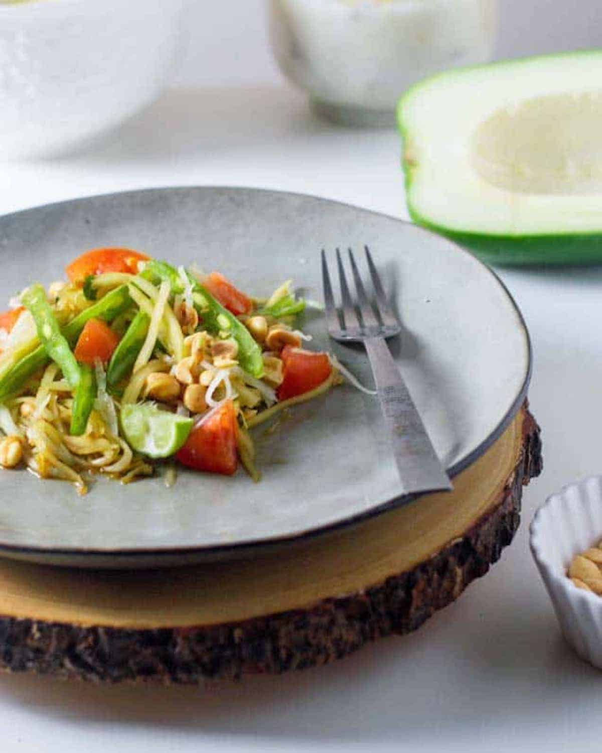 Side view of a plate of green papaya salad with tomatoes.