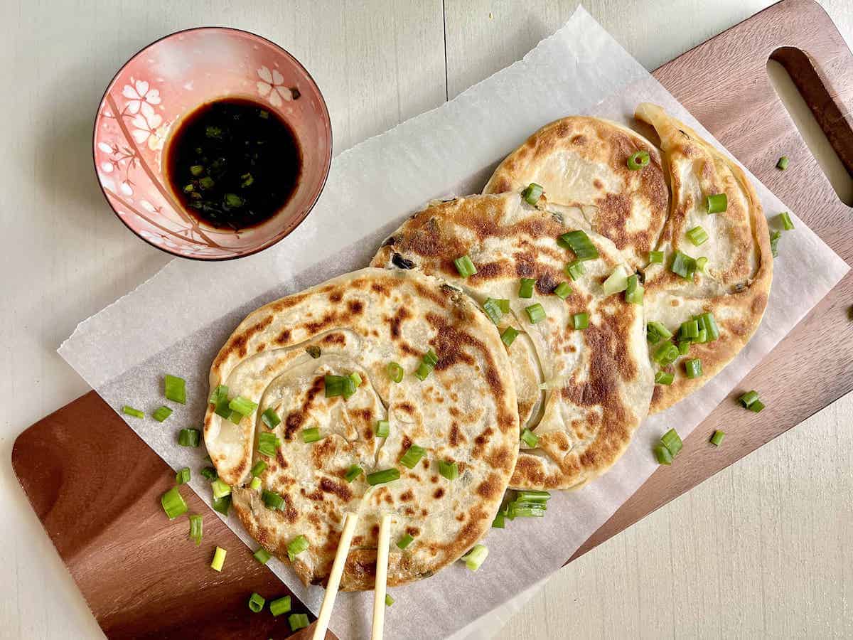 3 golden crispy spring onion pancakes on a wooden platter.