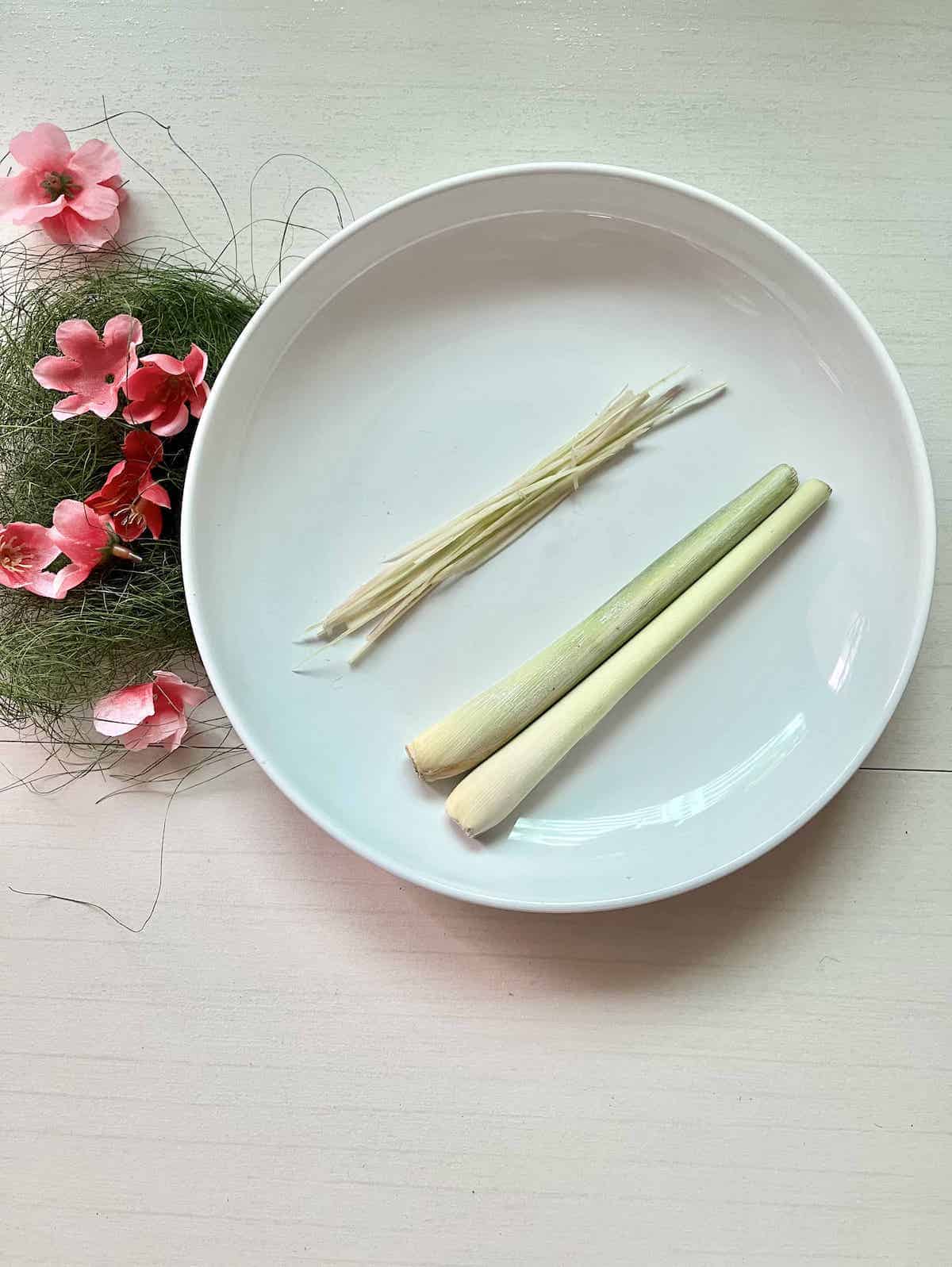 Sliced lemongrass and whole lemongrass on a white plate.