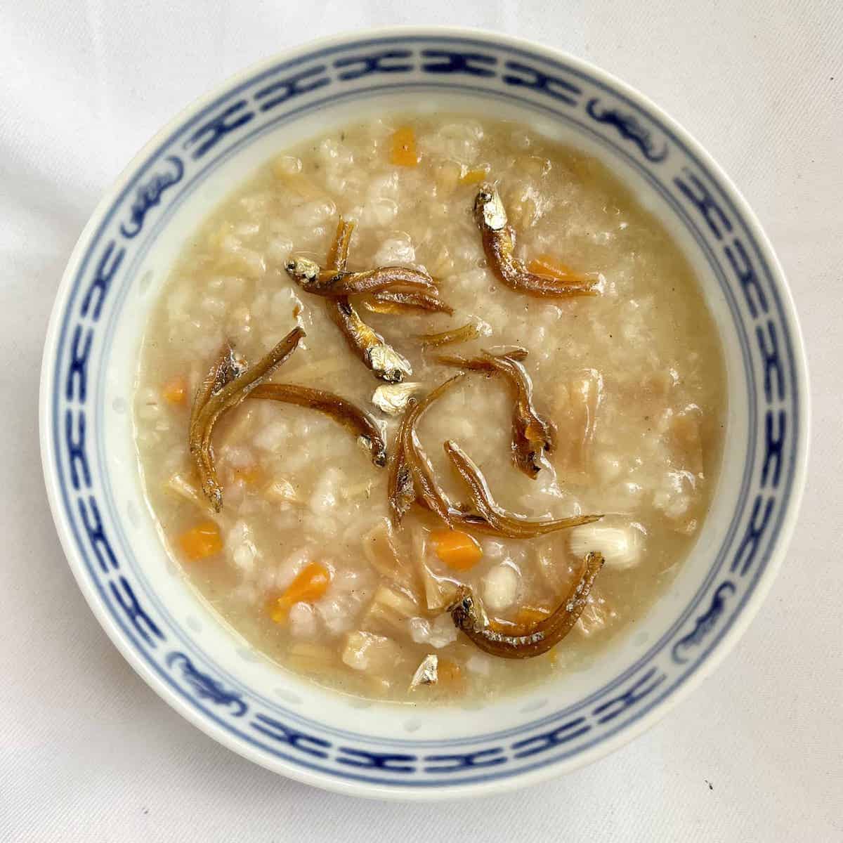 A bowl of rice congee with fried fish on top.