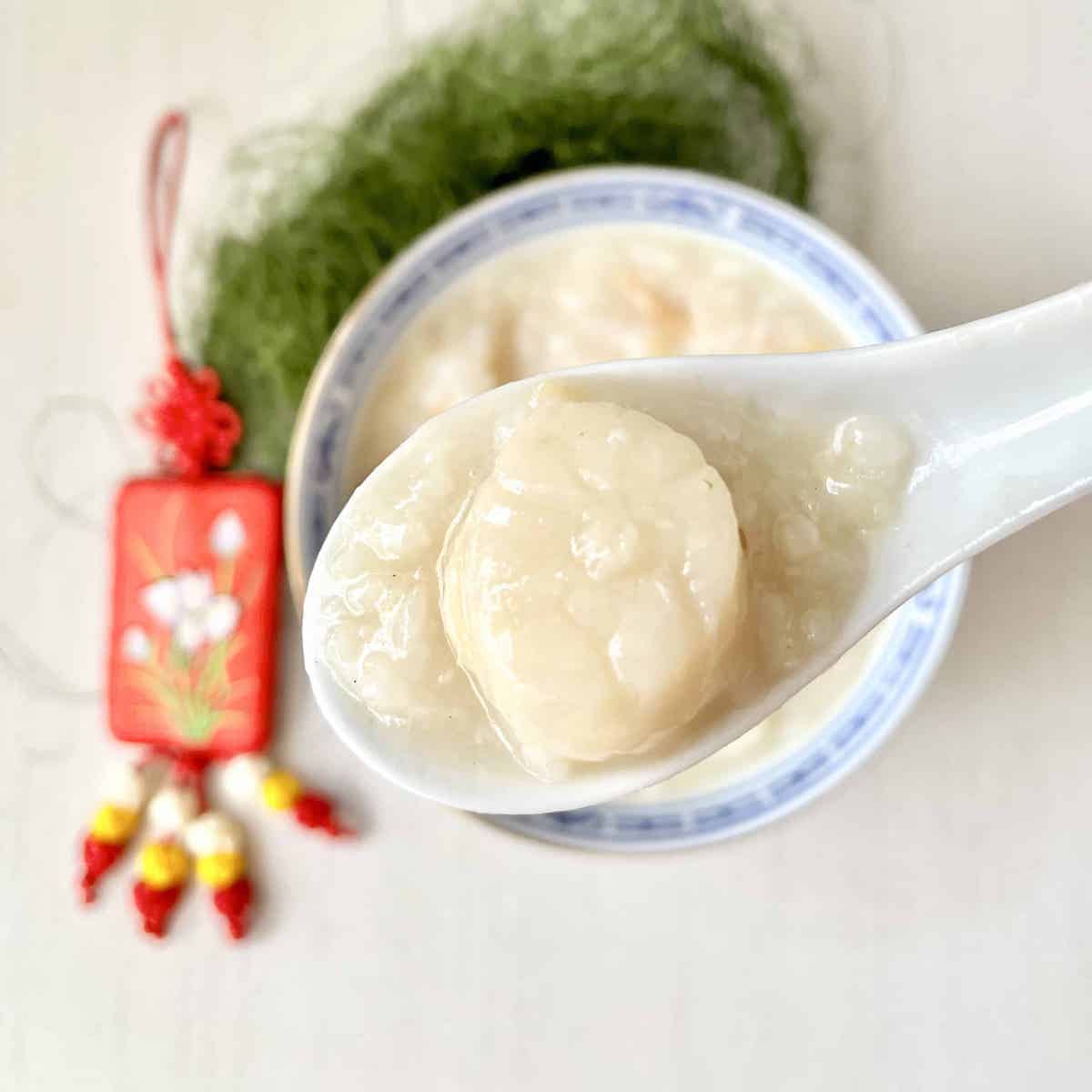 A spoon scooping a fresh scallop out of a bowl of seafood congee.