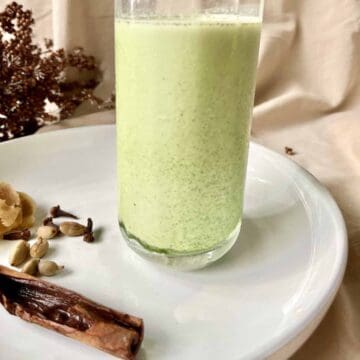 A glass of cold Matcha Chai Latte with Masala Chai spices next to it.