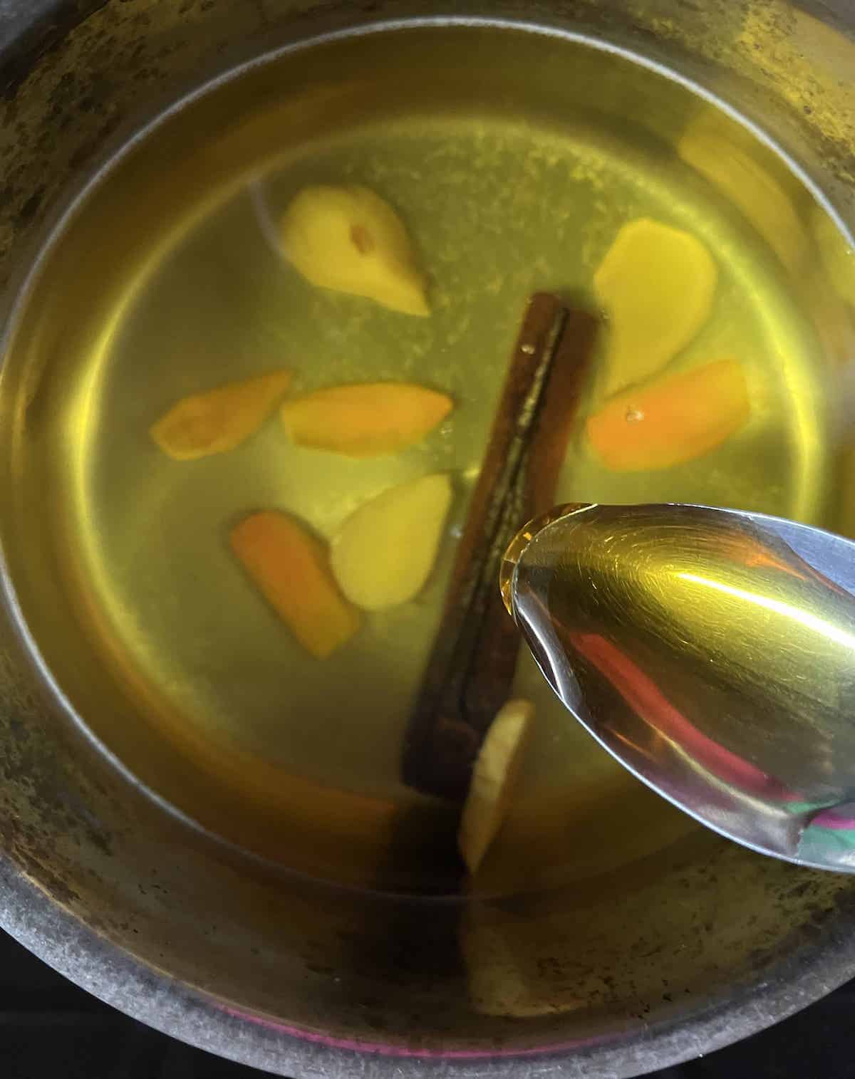 Stirring honey into a pot of ginger turmeric cinnamon tea with lemon juice.