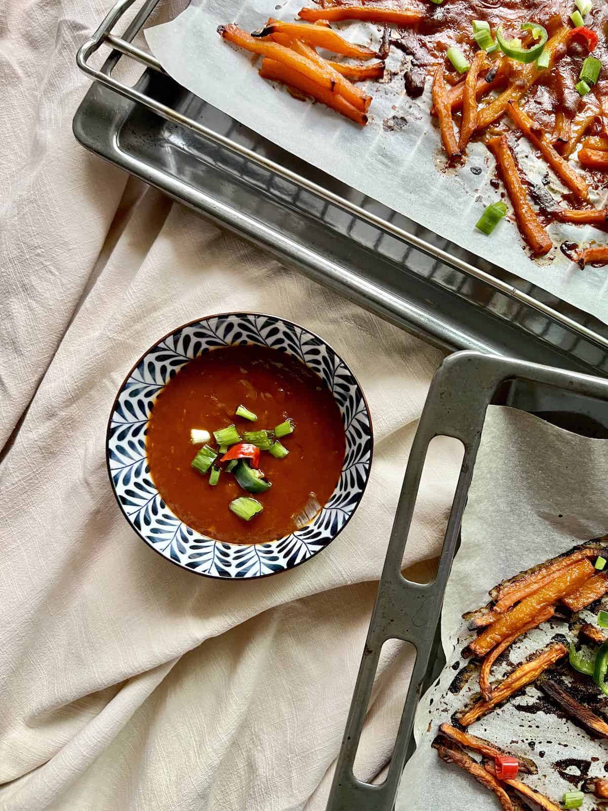 A bowl of gochujang sauce with 2 trays of roasted butternut squash around it.