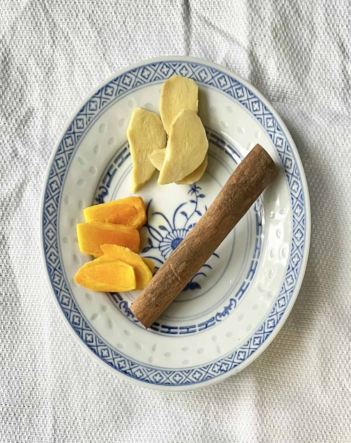 Slices of ginger and turmeric next to a cinnamon stick.