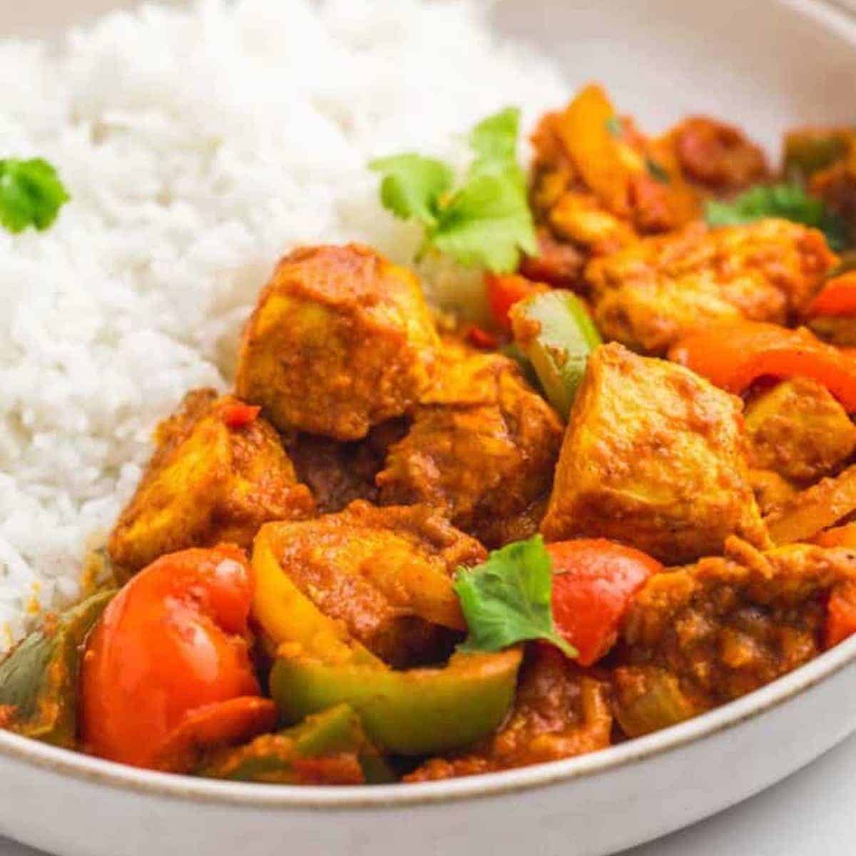 Close-up of orange chicken jalfrezi curry with white rice on a white plate.