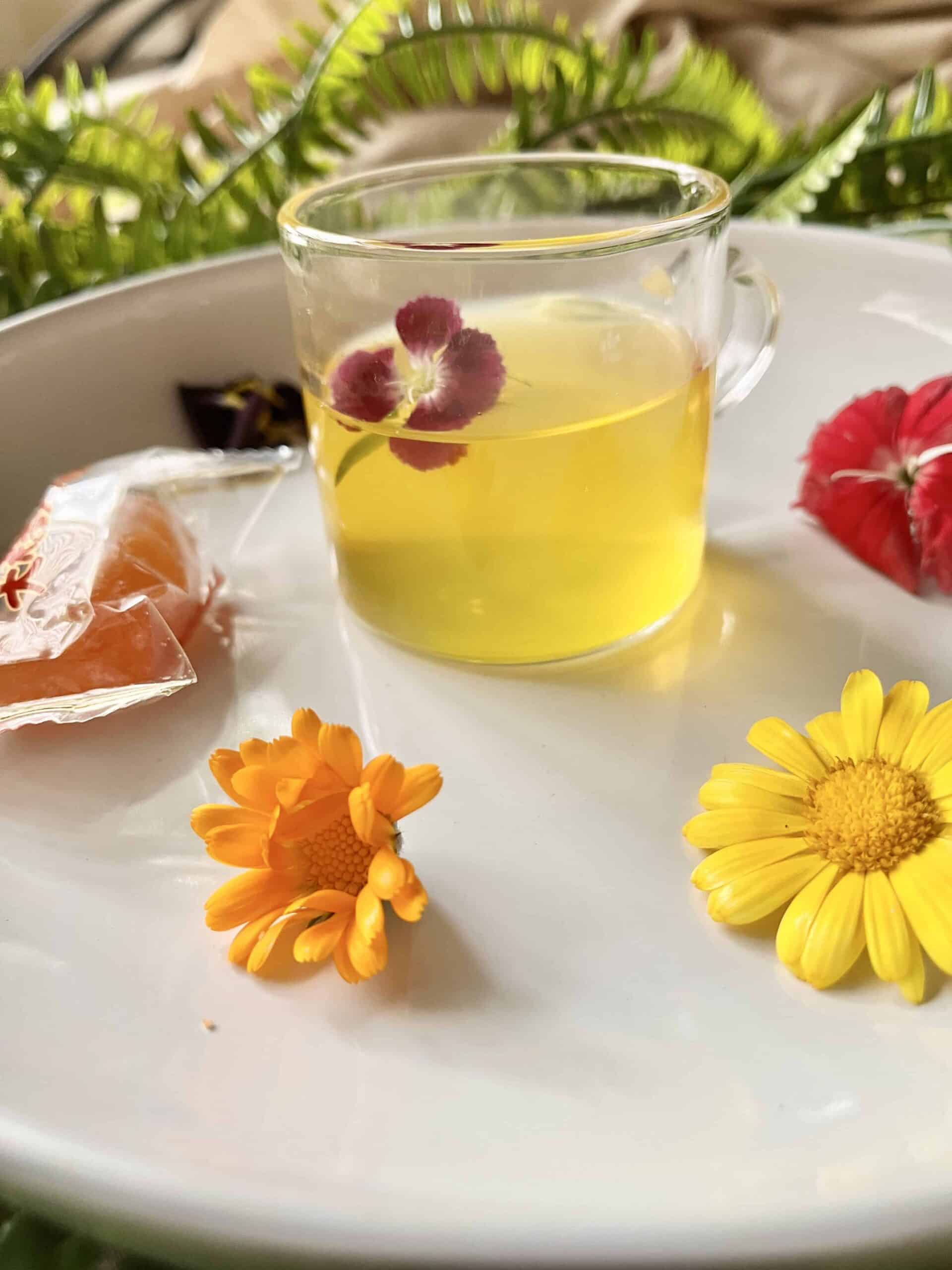 A cup of turmeric ginger cinnamon tea with lemon and honey amongst edible flowers.