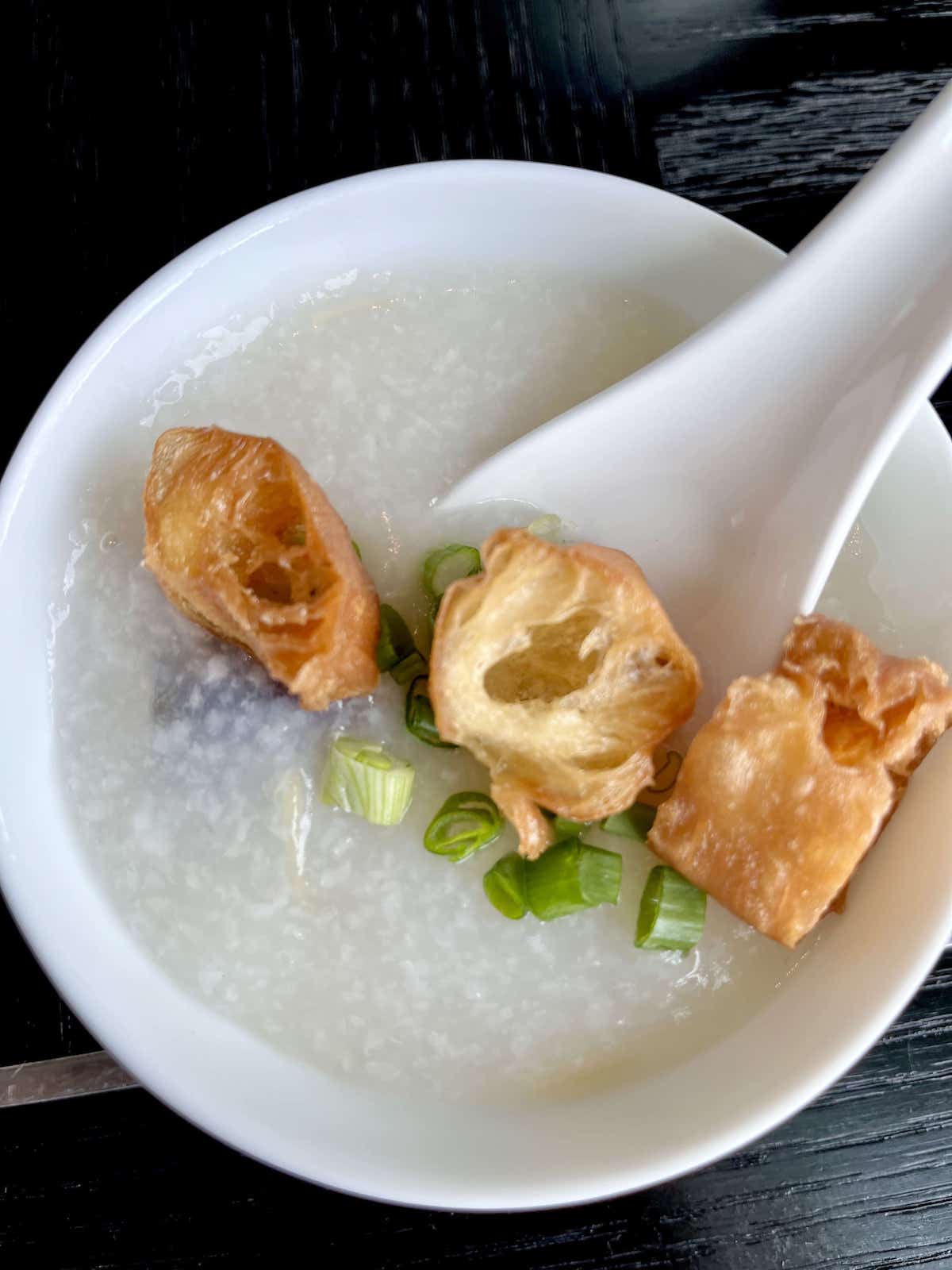 Overheat shot of a bowl of rice porridge and fried you tiao and scallions on top.