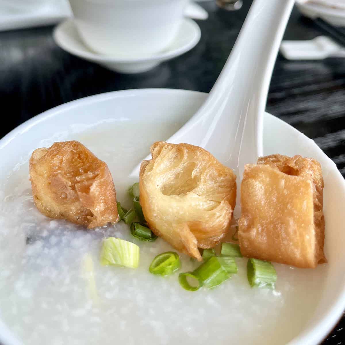 Close-up of a bowl of Cantonese congee topped with you ciao and scallions.