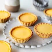 3 golden egg tarts on a plate, surrounded by 3 more off the plate.